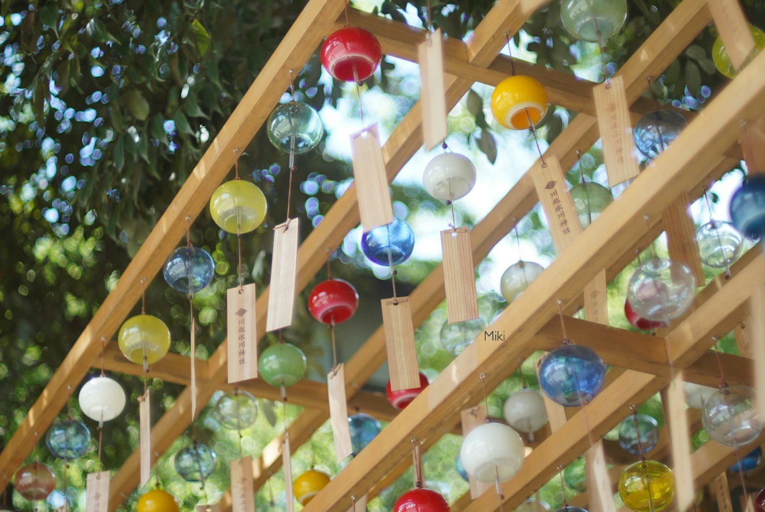 Bunte Windspiele hängen von einer Holzstruktur unter Grün