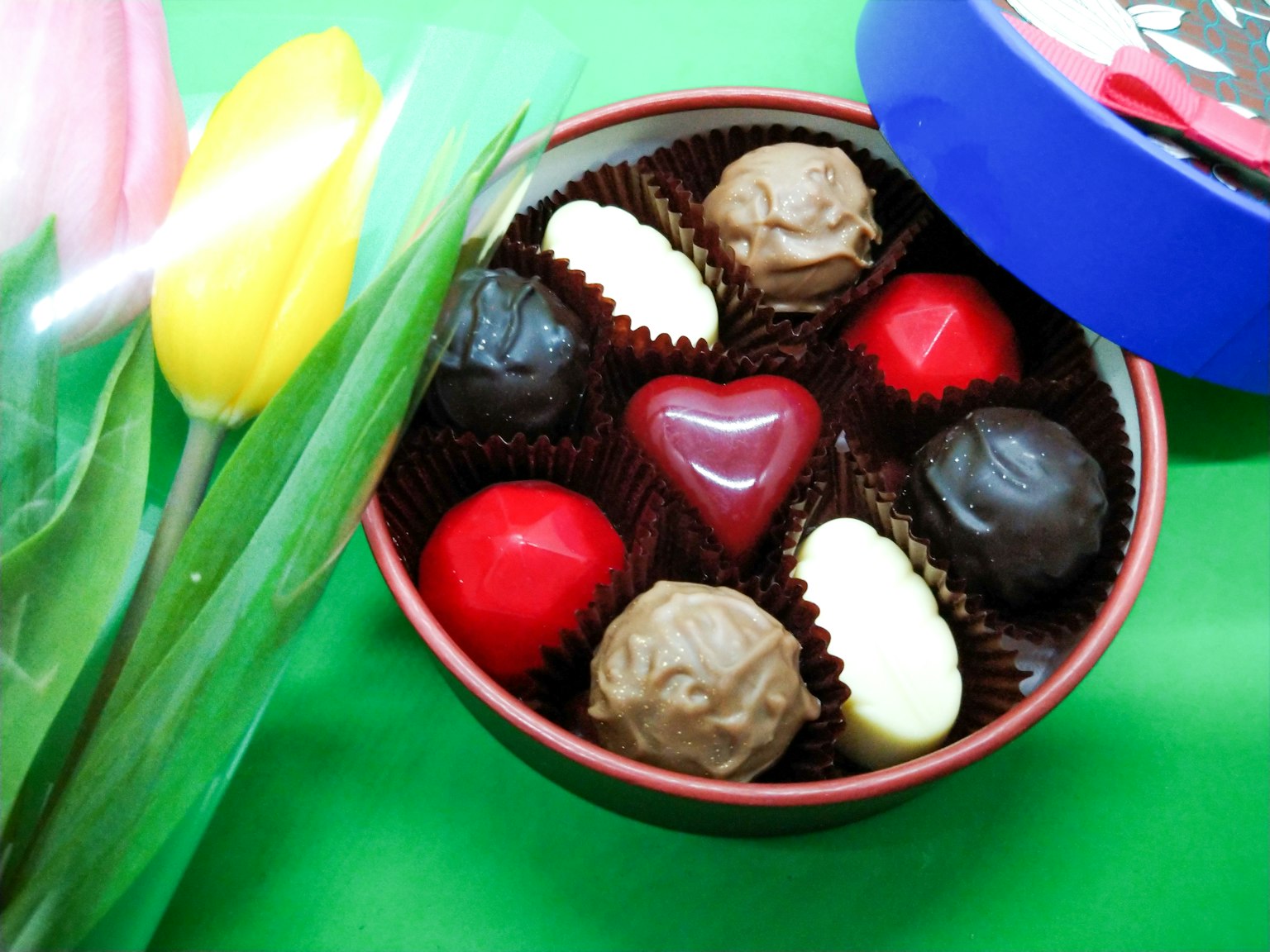 Một hộp sô cô la đa dạng bao gồm một viên sô cô la hình trái tim đỏ cùng với hoa tulip đầy màu sắc