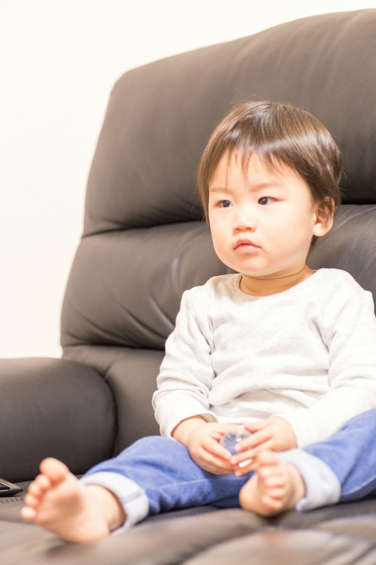 Un bambino piccolo seduto su un divano nero con un'espressione seria