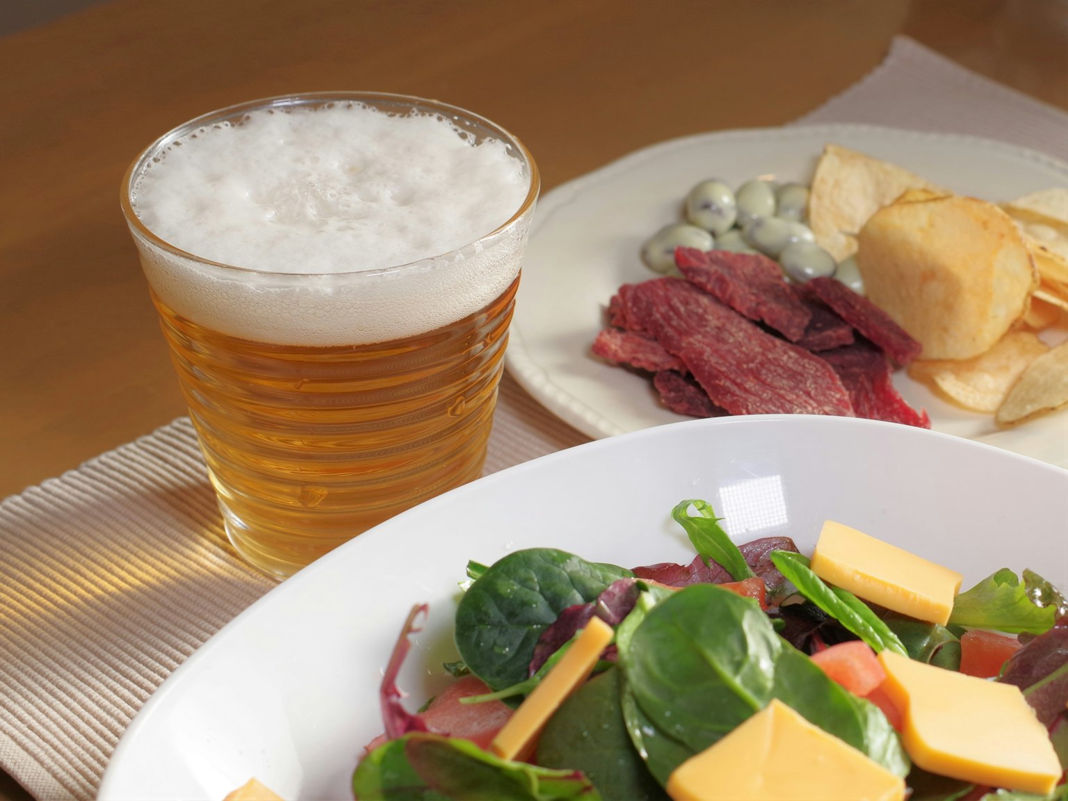 Une salade colorée avec du fromage accompagnée d'un verre de bière et de collations variées