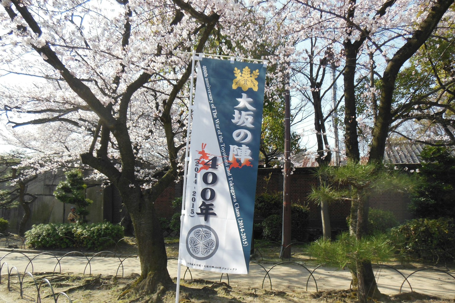 Spanduk biru di bawah pohon sakura dengan tulisan Dazaifu dan peringatan 100 tahun