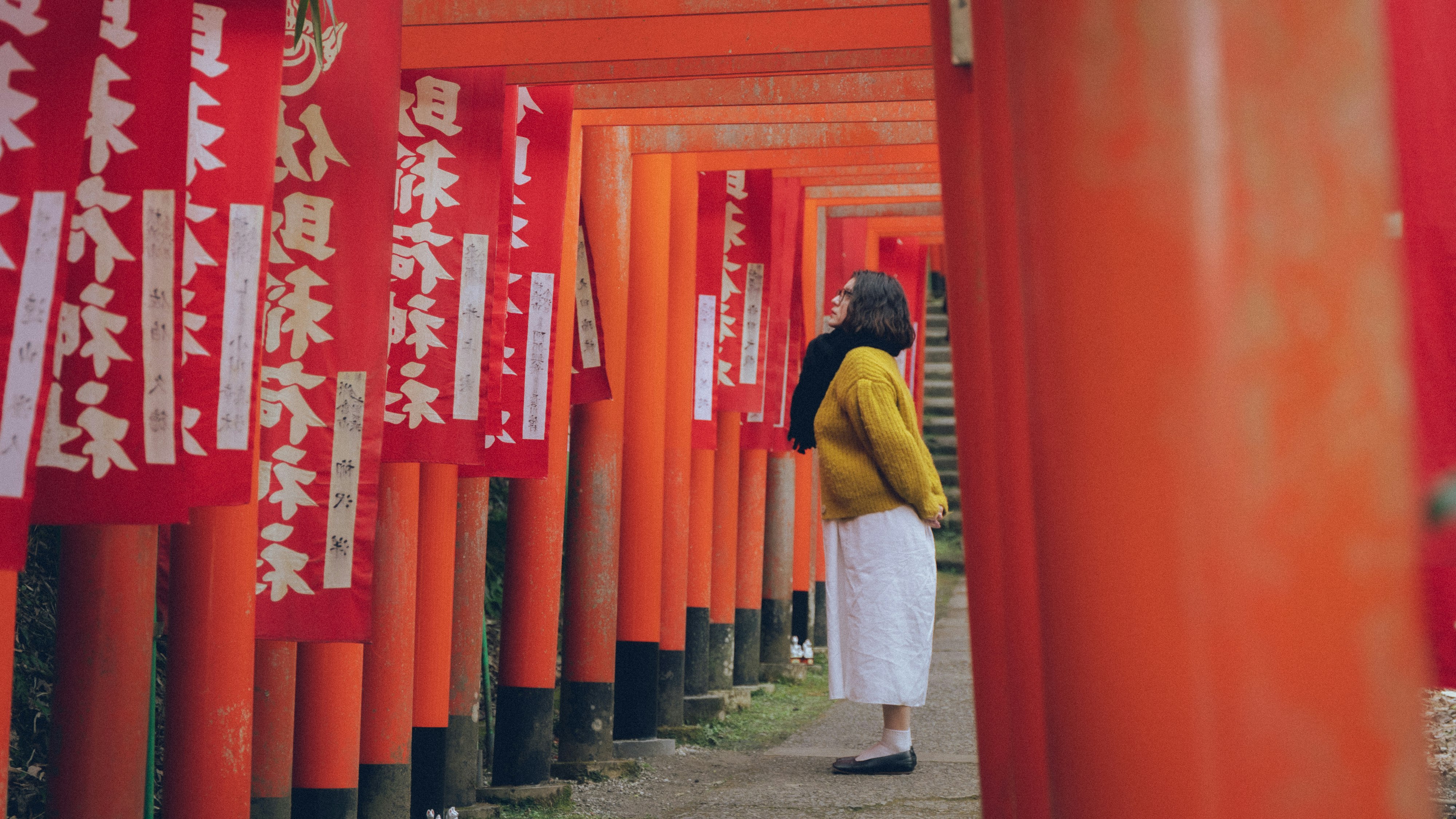 Woman walking along a path lined with vermilion torii gates, seen through red pillars