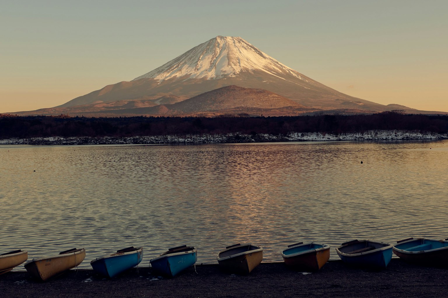 Mount Fuji towering over a tranquil lake at sunset with colorful boats in the foreground