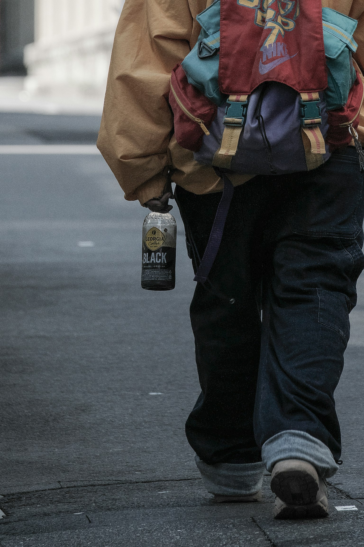 Eine Person, die auf der Straße geht und ein Getränk hält, trägt einen bunten Rucksack