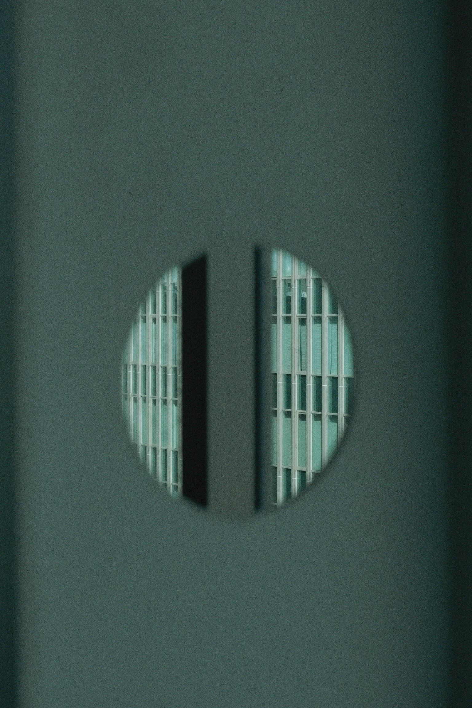 Round opening in a green wall revealing vertical striped windows of a building