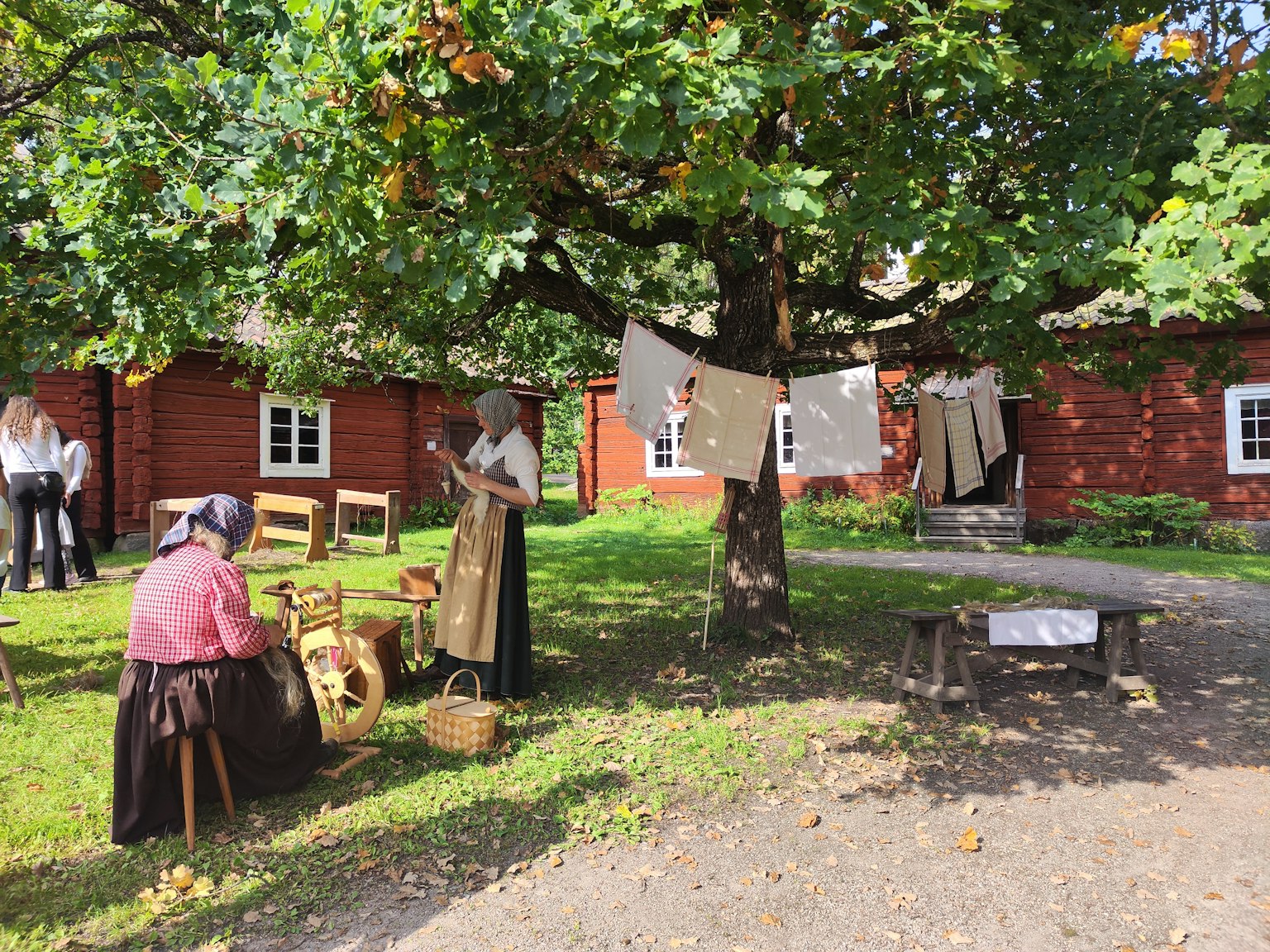 Scène de personnes en tenue traditionnelle rassemblées sous un arbre devant des maisons rouges