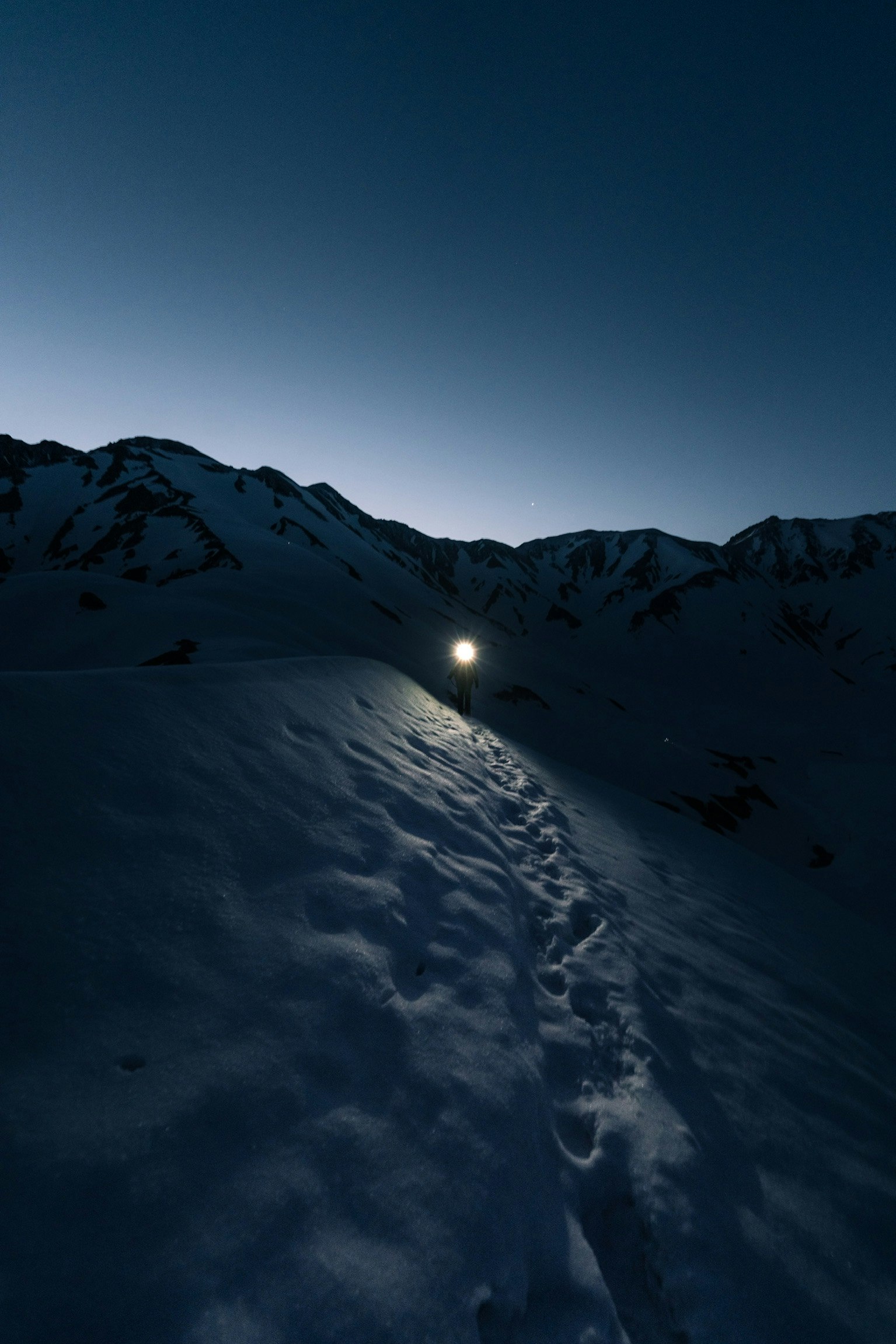 雪山の稜線を照らす小さなライトのある夜の登山道