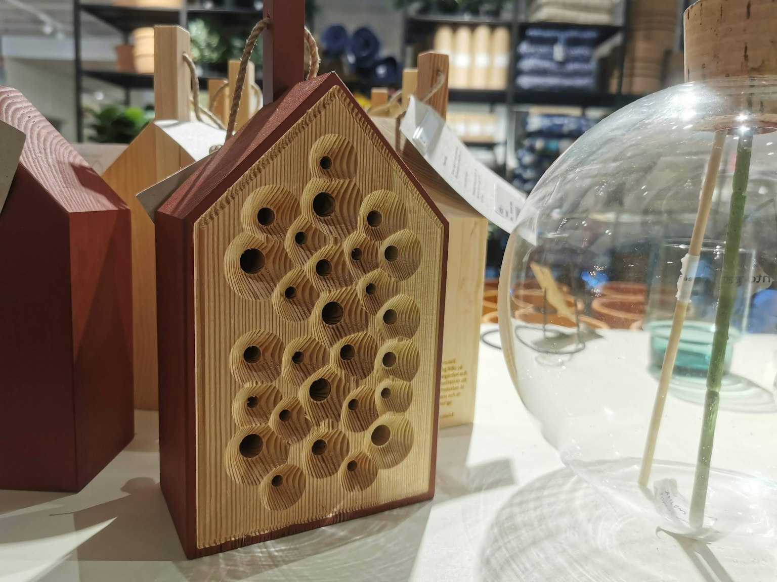Hotel per insetti in legno a forma di casa con diversi fori accanto a un oggetto in vetro trasparente