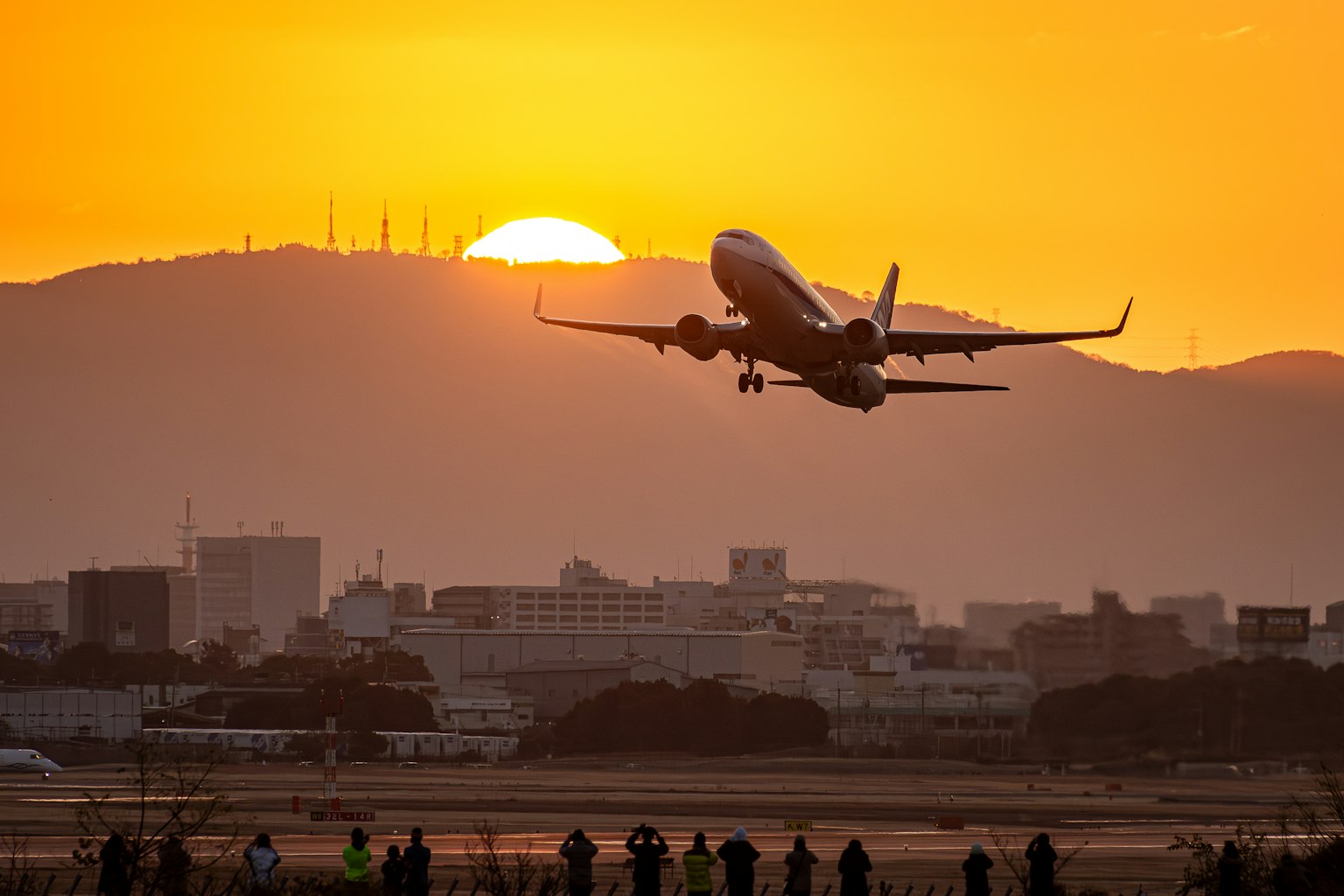 Airplane taking off against a sunset with silhouettes of spectators