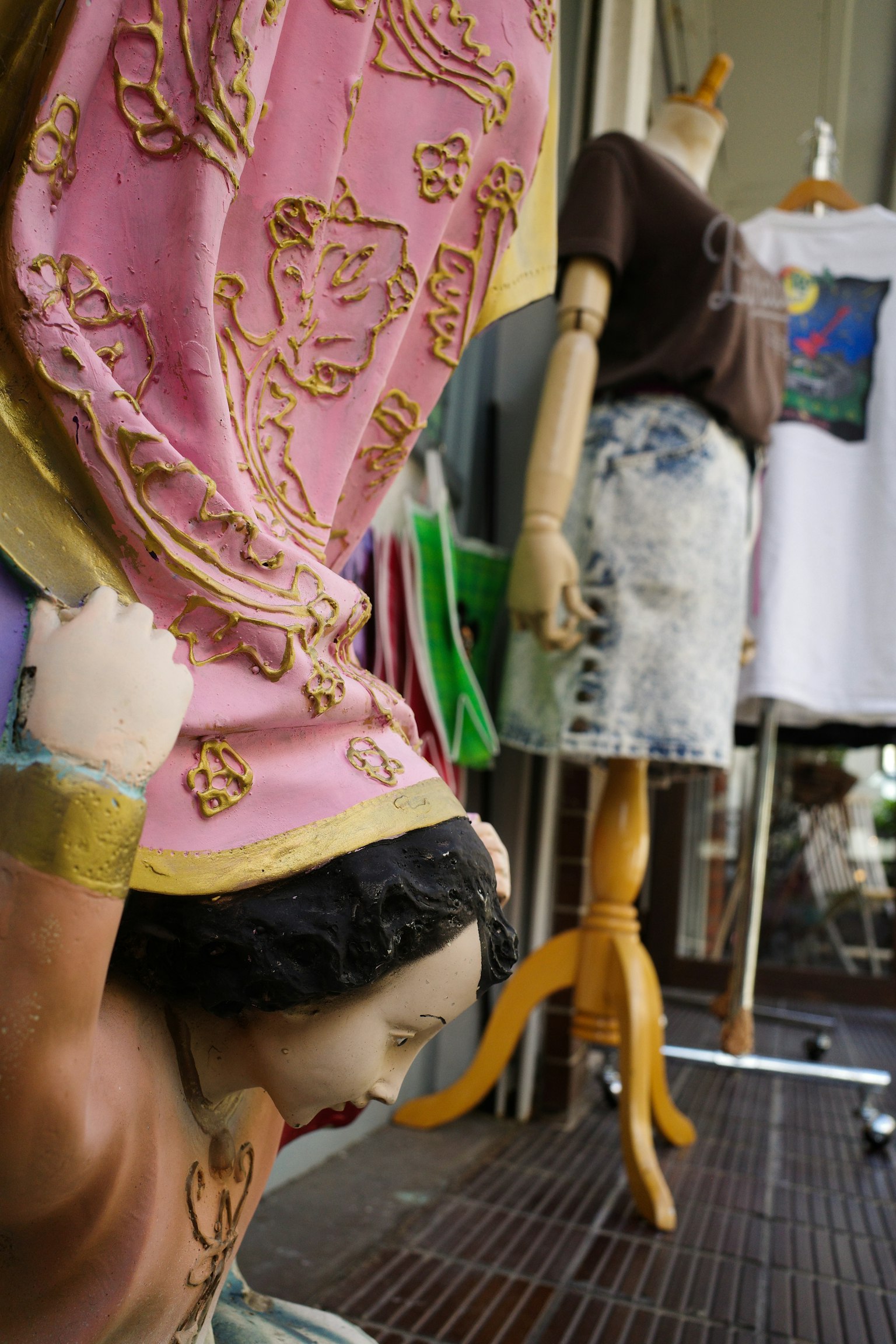 ตุ๊กตาที่แต่งตัวสีสันสดใสอยู่ในพื้นหน้าและมีหุ่นโชว์เสื้อผ้าอยู่ในพื้นหลัง