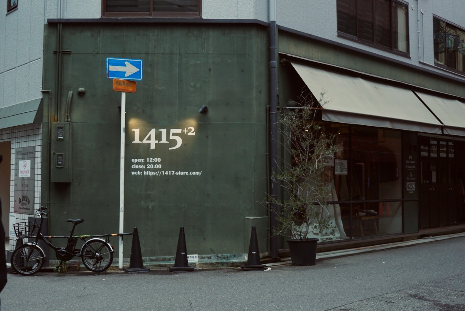 Eksterior toko dengan dinding hijau menampilkan nomor 1415 sepeda dan papan jalan terlihat
