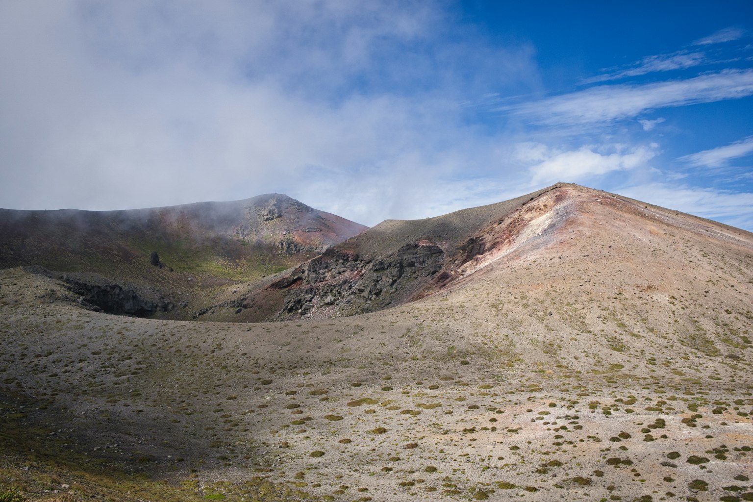 Paesaggio vulcanico con cielo blu e nuvole, terreno arido con vegetazione sparsa