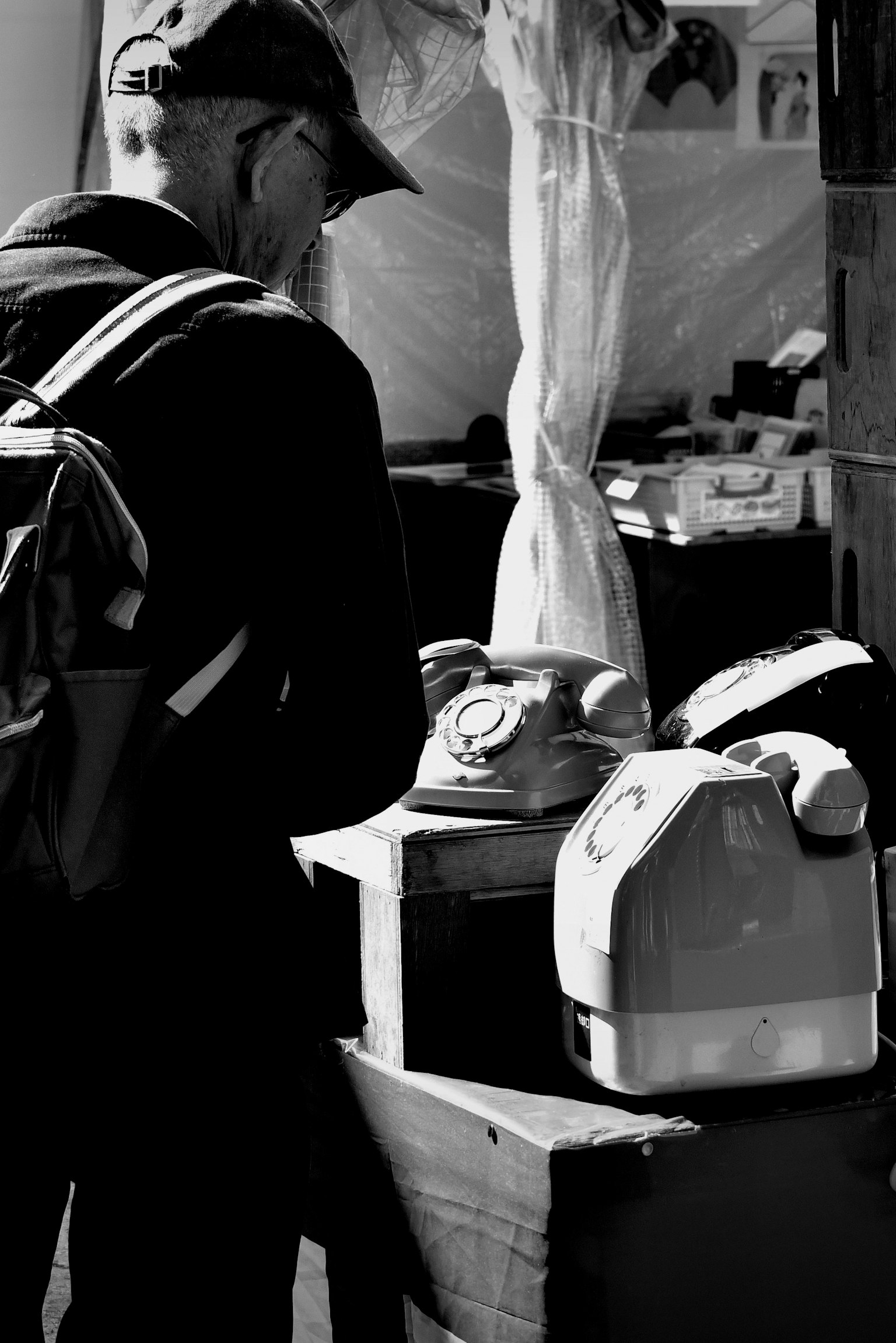 男性が古い電話機を見つめるモノクロ写真