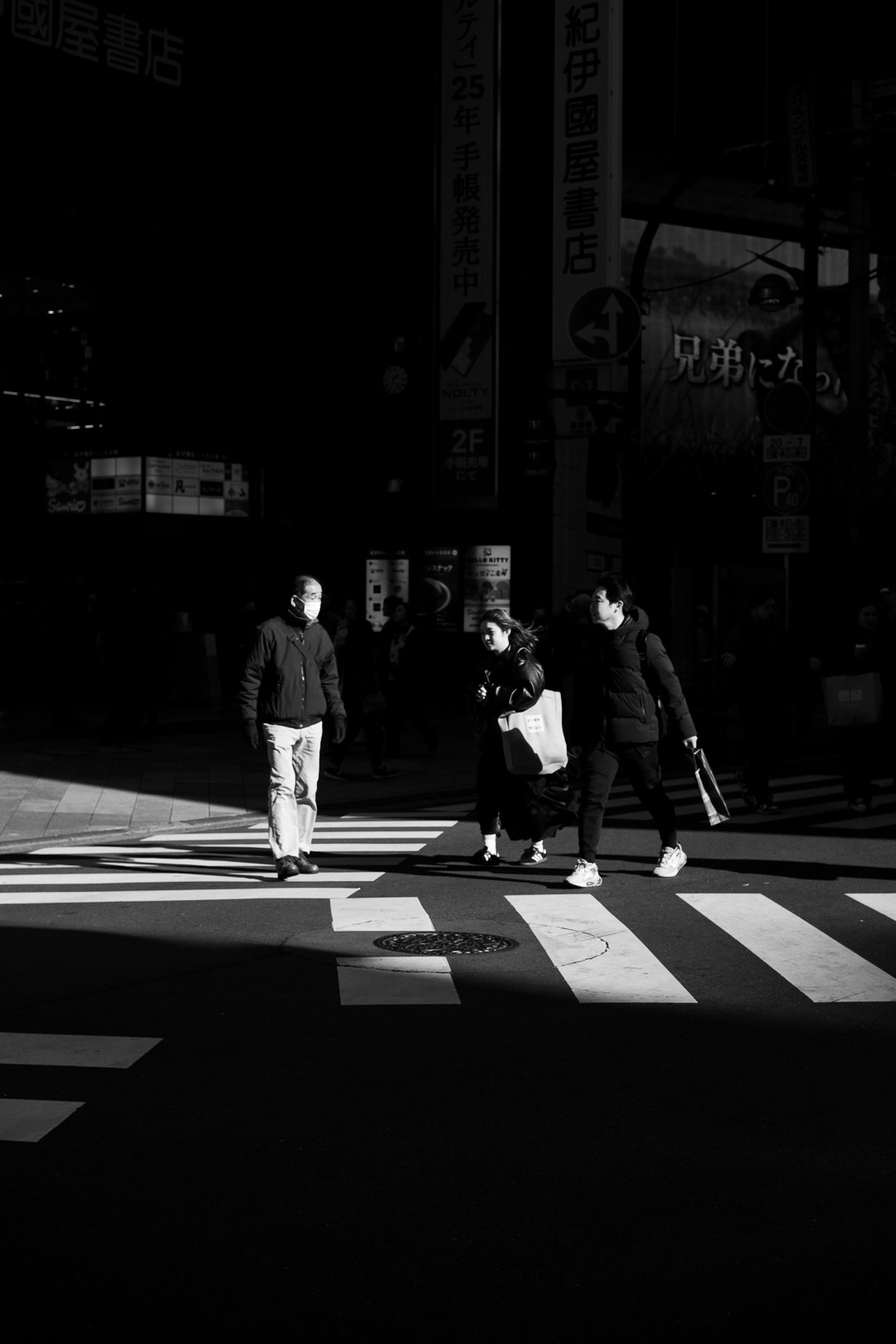 光が差し込む横断歩道を歩く人々のモノクロ街景