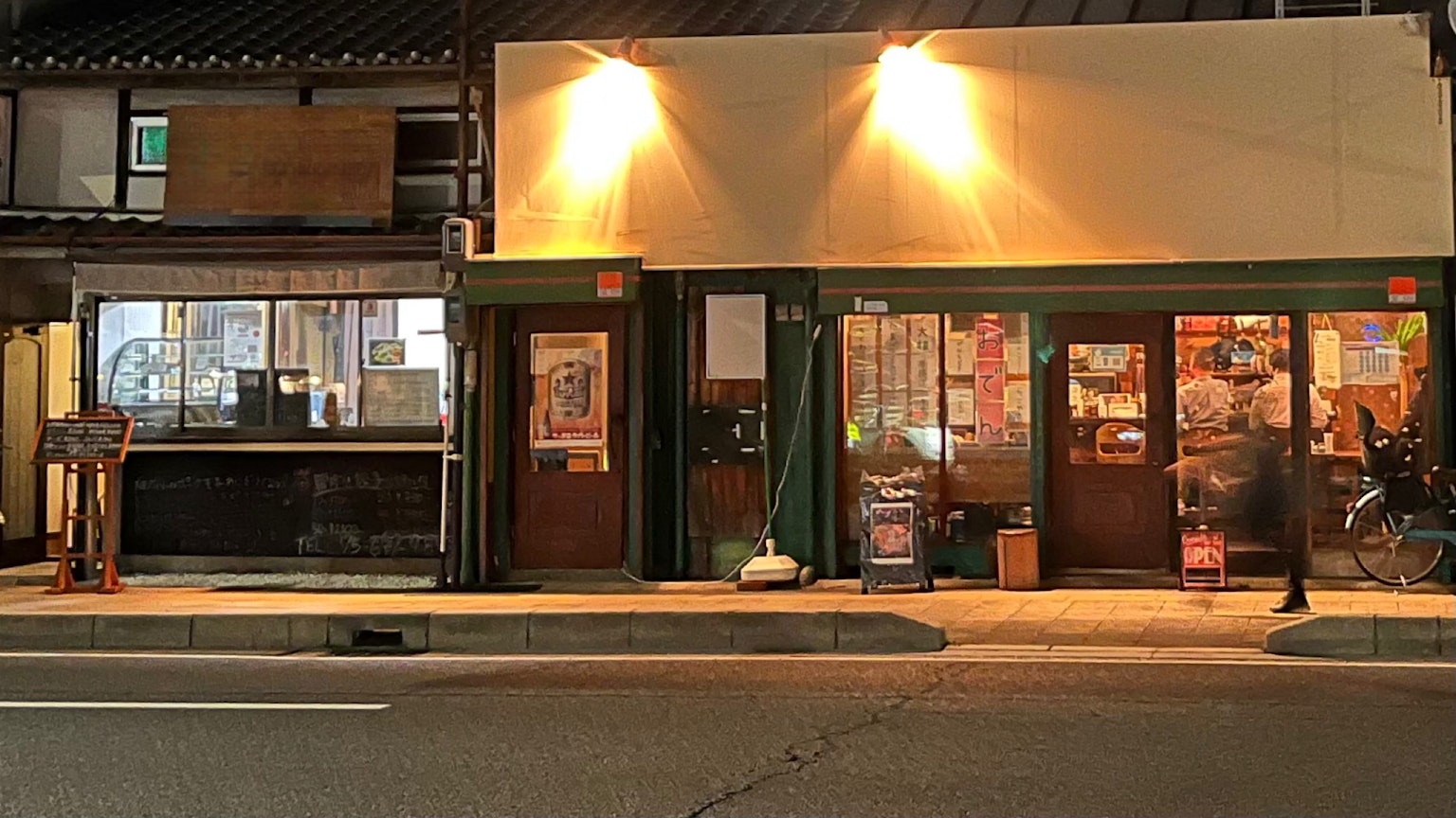 A storefront with green exterior and bright lights in a night shopping street
