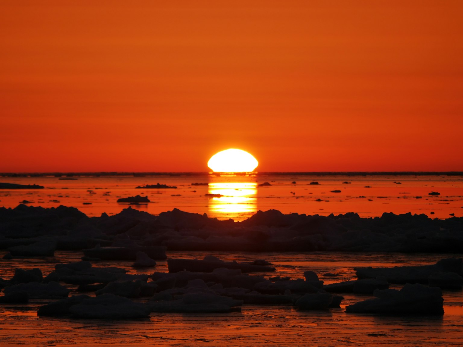 Coucher de soleil orange vif sur l'océan avec des morceaux de glace au premier plan