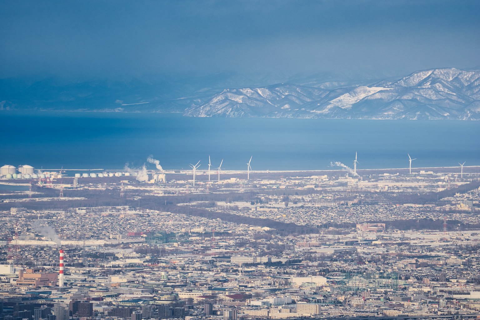 Paesaggio urbano con turbine eoliche montagne e mare sullo sfondo