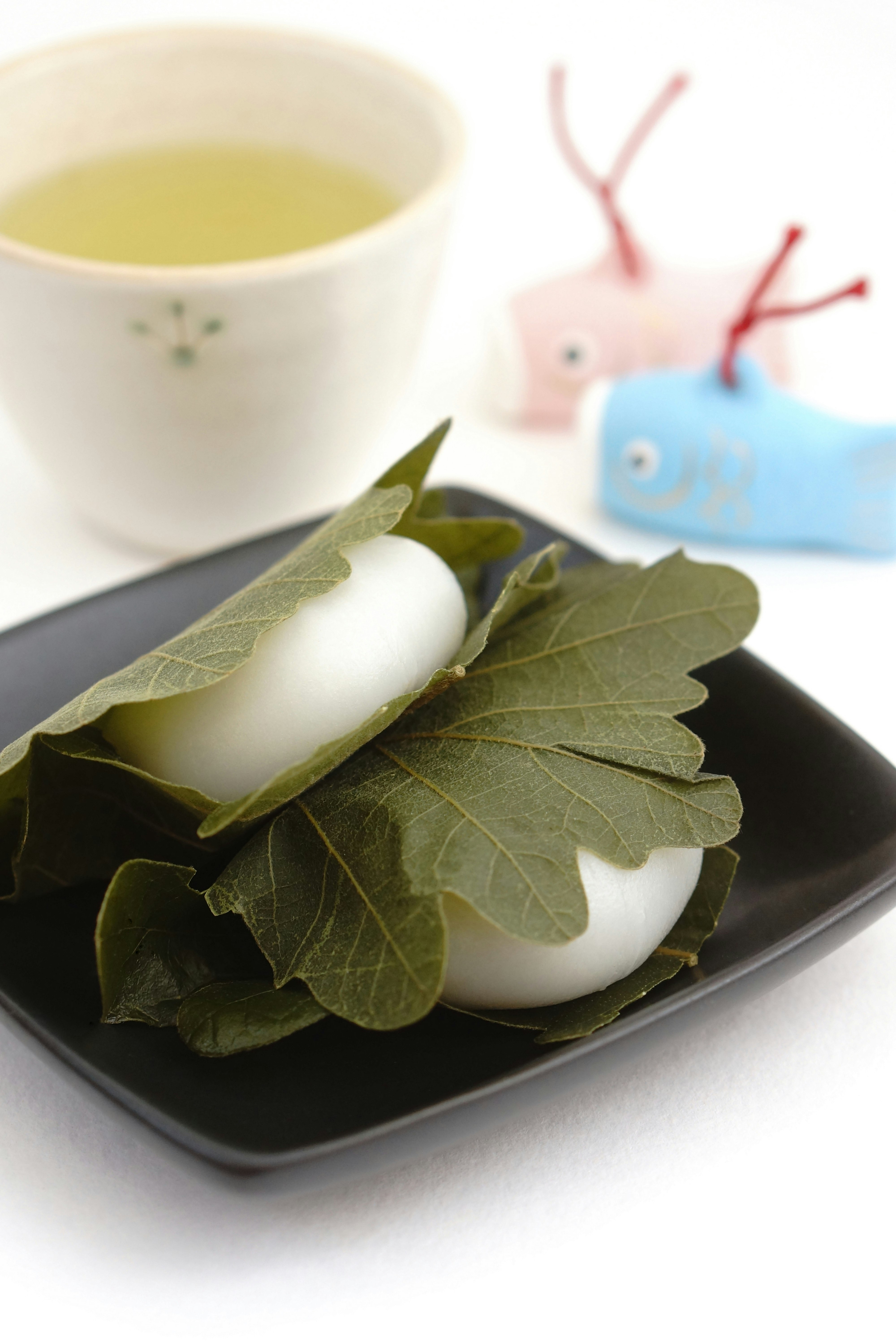 白い餅と柏の葉の和菓子、湯気のあるお茶添え