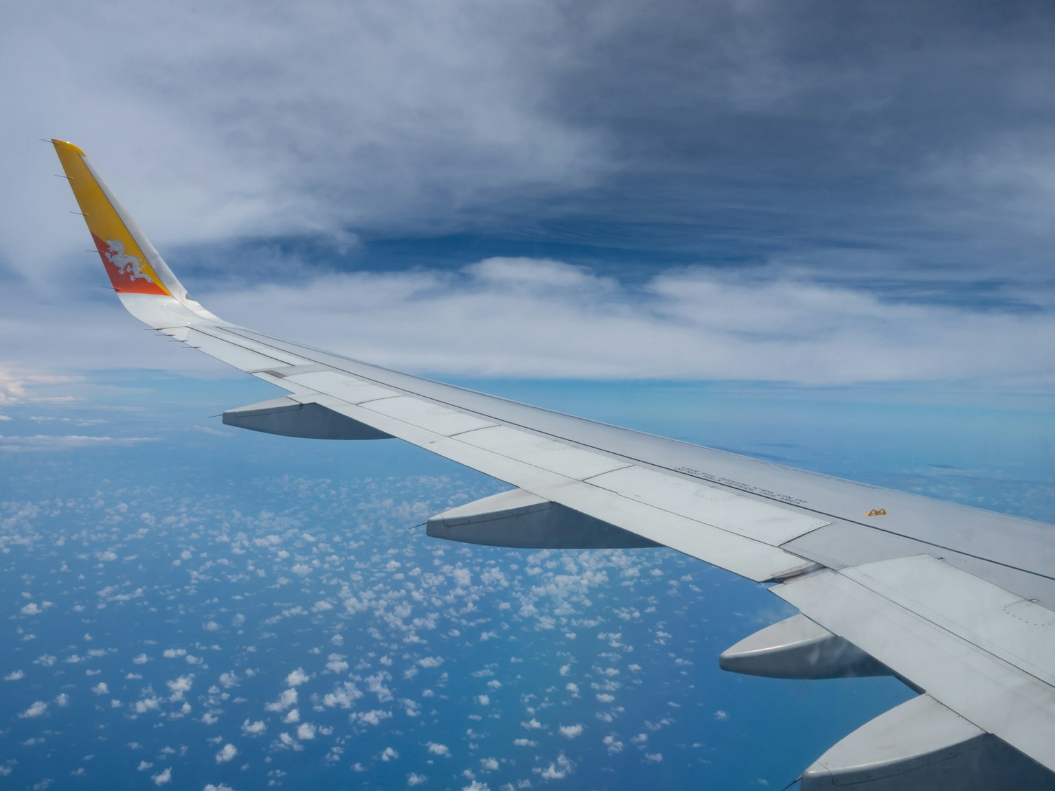 Ala di un aereo con nuvole e vista sull'oceano blu