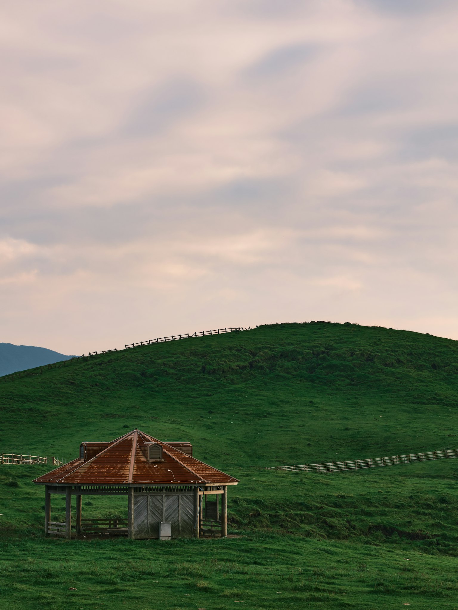 Ancienne cabane devant des collines vertes sous des nuages doux