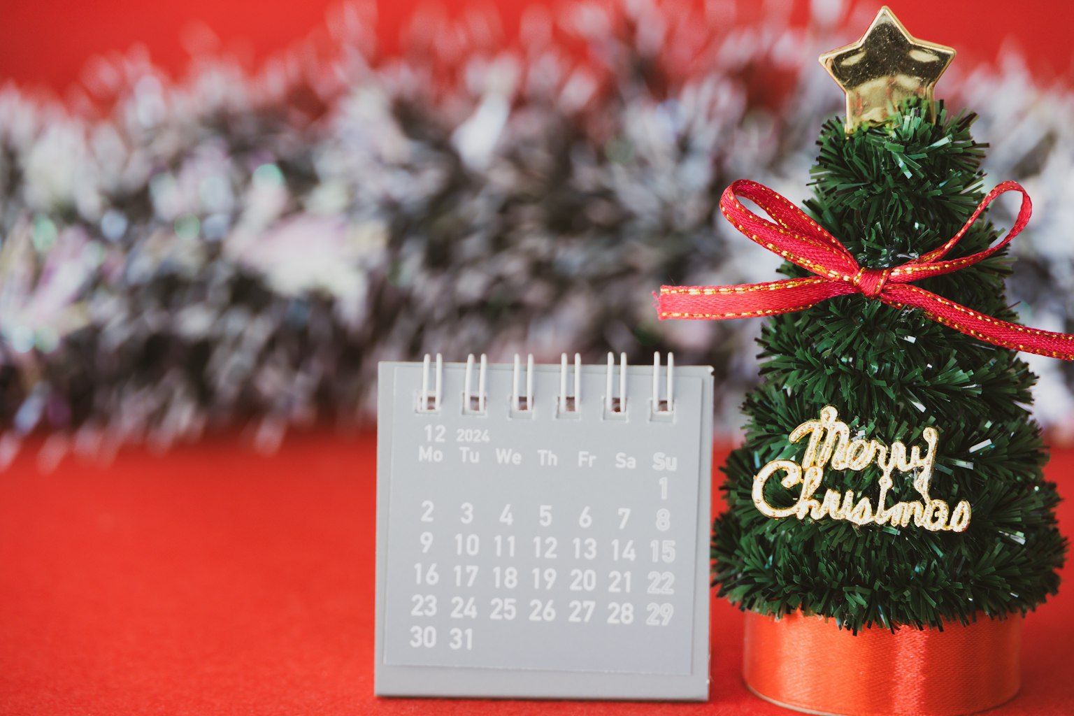 Ein kleiner Weihnachtsbaum mit einem Kalender auf rotem Hintergrund mit einer silbernen Girlande