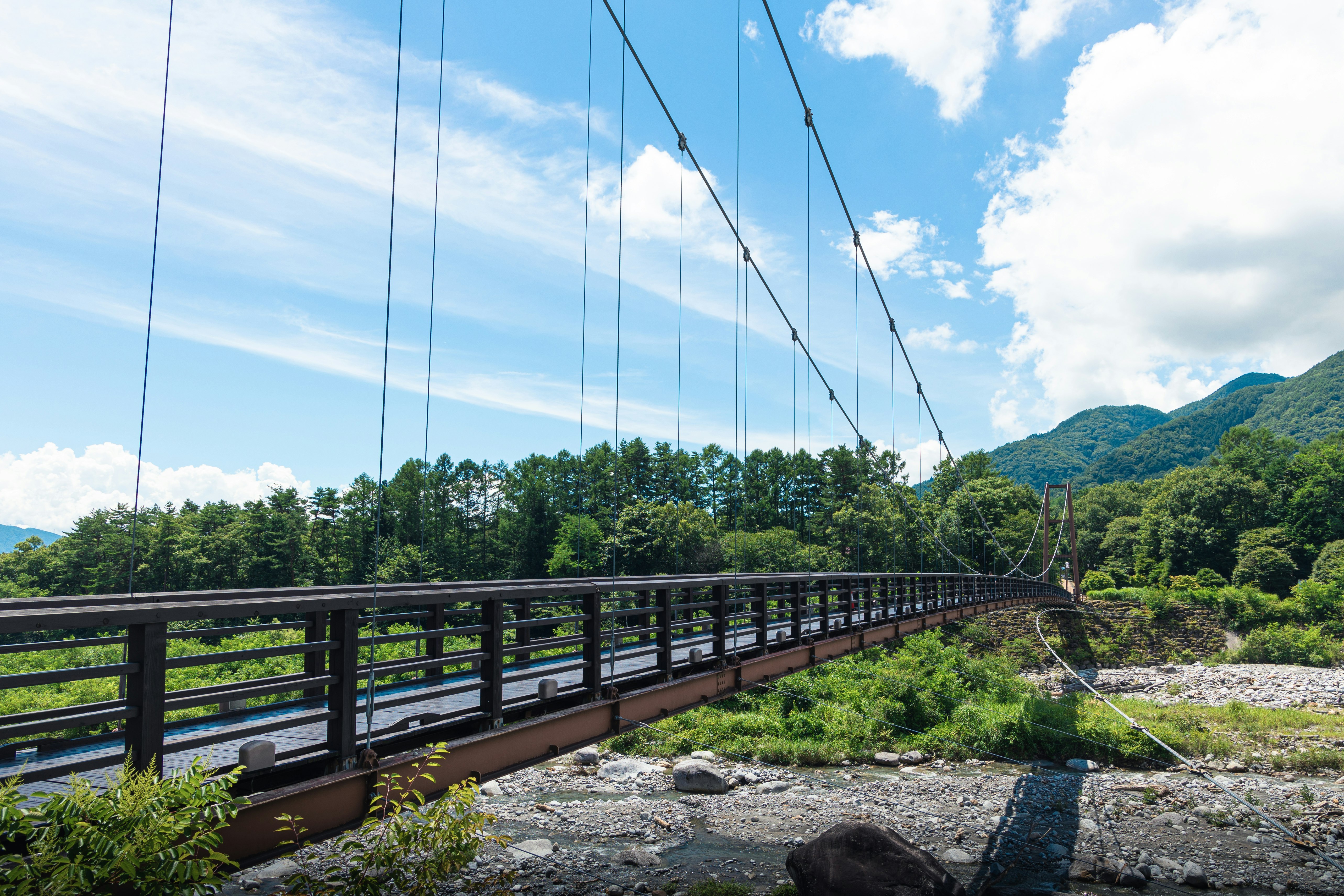 vue d’un pont suspendu au-dessus d’une rivière et de montagnes vertes