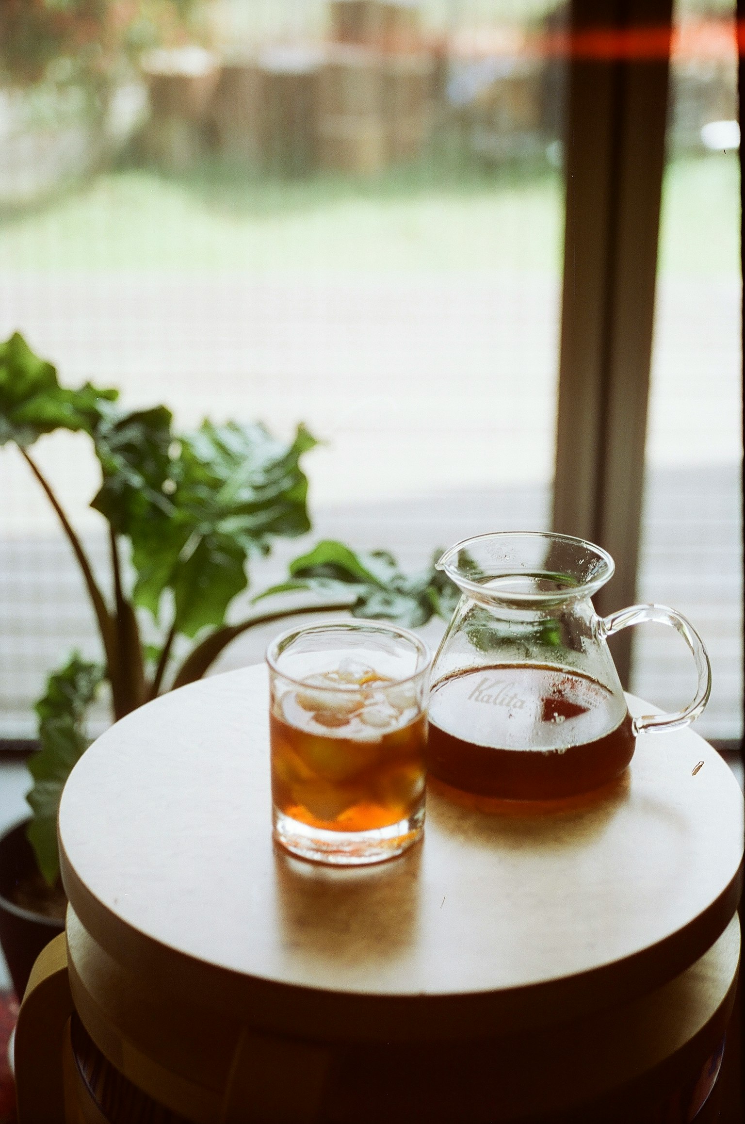 木桌上的冰茶杯和壶 窗外可见绿植