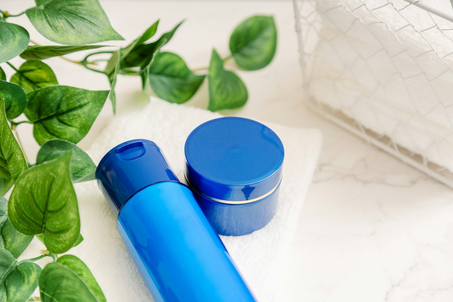 Image de bouteilles de cosmétiques bleues et d'un pot de crème avec des plantes vertes en arrière-plan