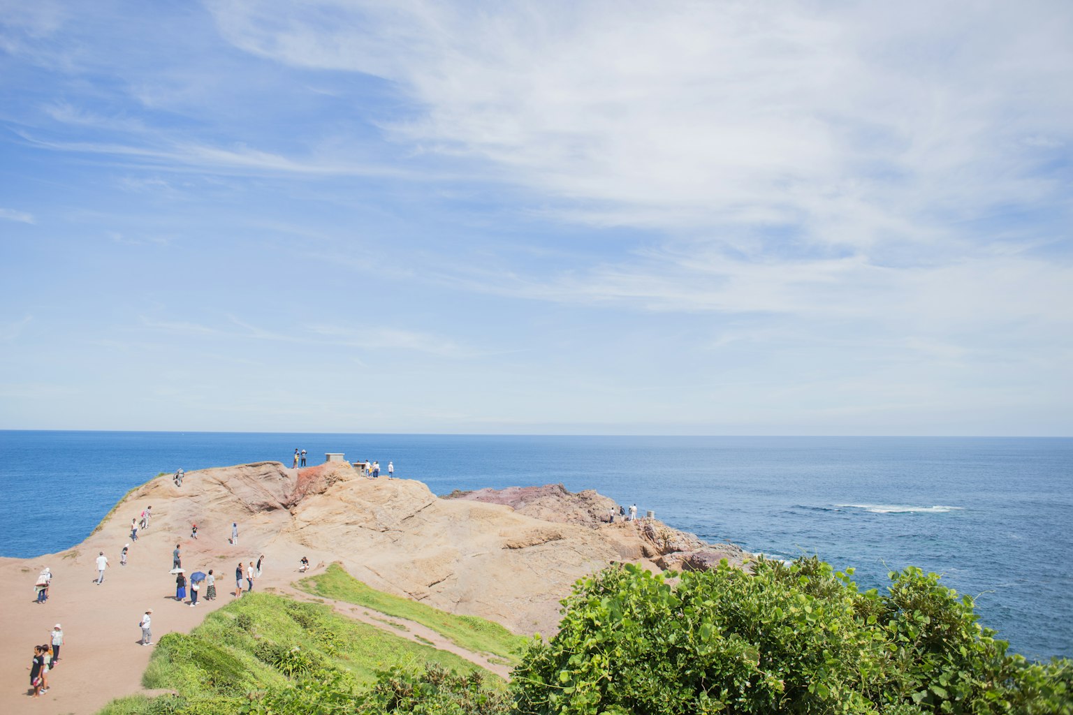 A scenic view of a green hill with people under a blue sky and ocean