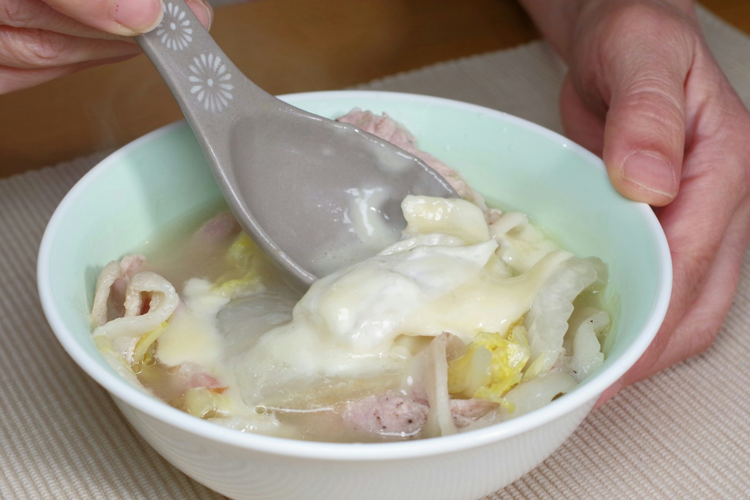 손이 밝은 녹색 그릇에서 수프를 뜨는 숟가락을 잡고 있는 이미지