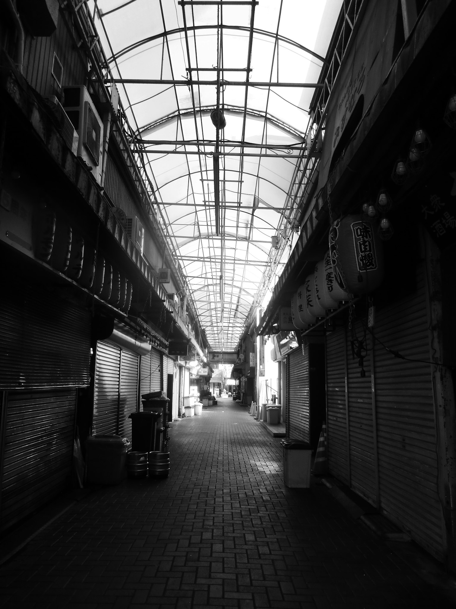 Black and white photo of a shopping street with a covered roof and closed shops