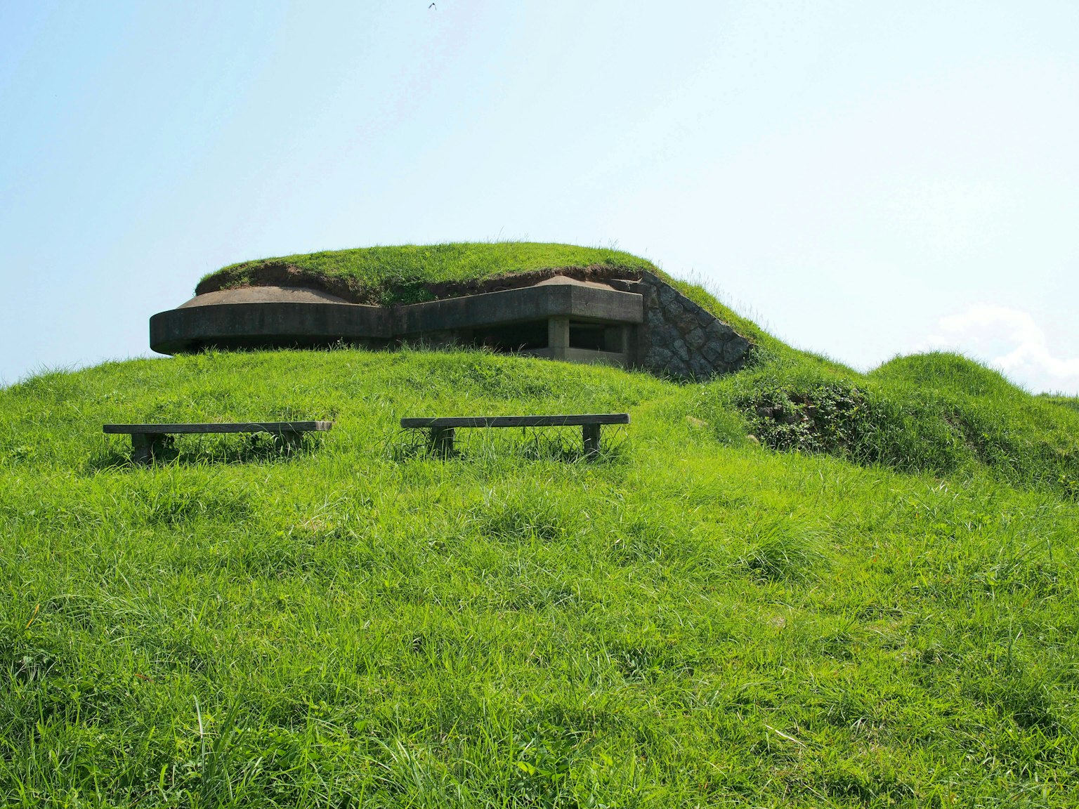 Tumulus ancien avec un abri au sommet entouré d'herbe verte luxuriante et de bancs