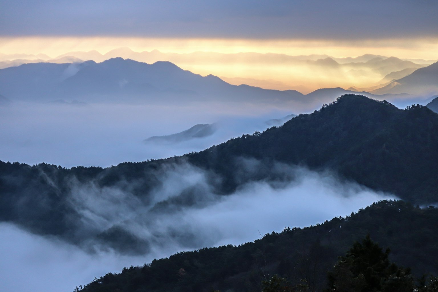 ภูเขาที่ถูกปกคลุมด้วยหมอกพร้อมพระอาทิตย์ขึ้นในพื้นหลัง