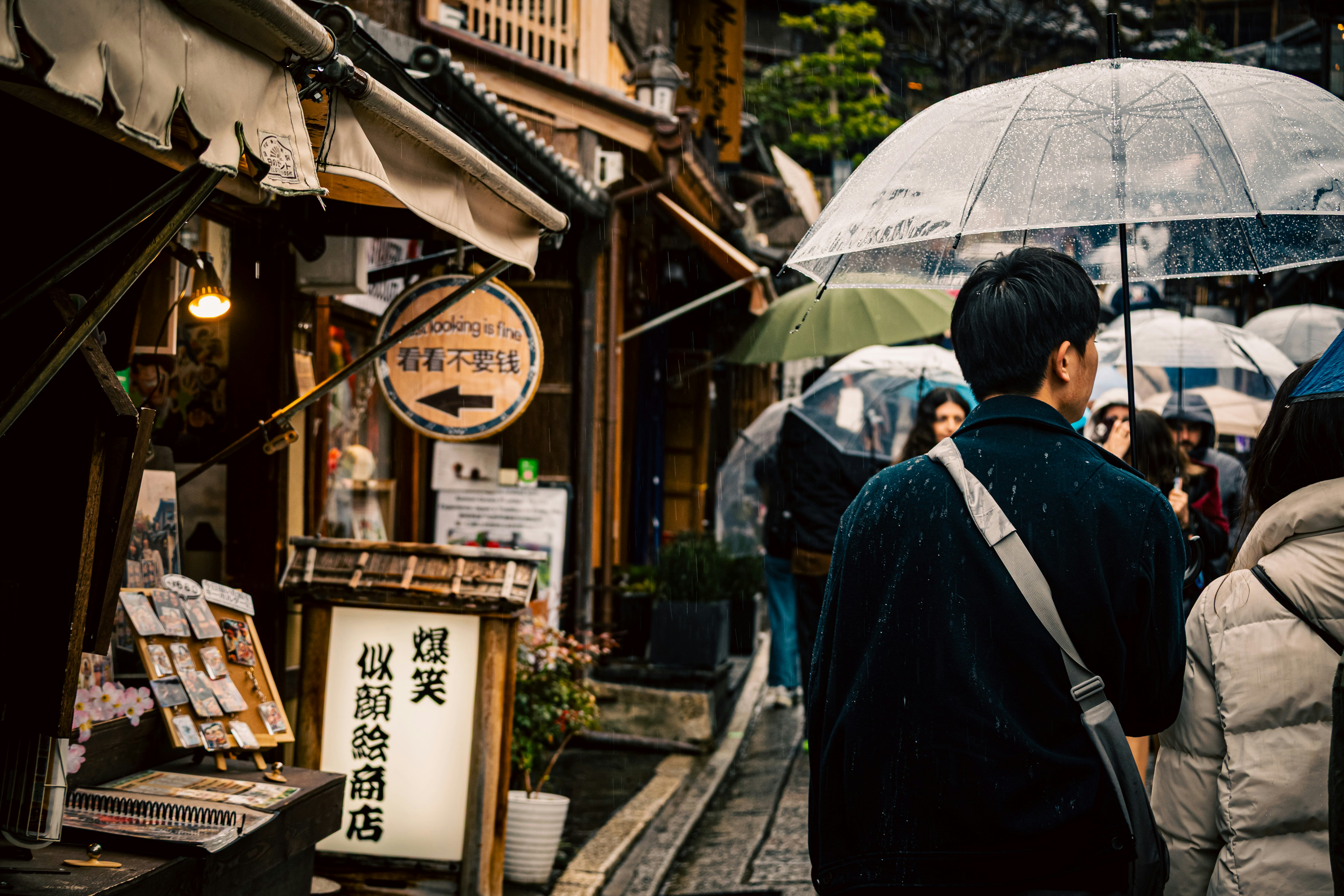 雨の路地で傘をさす人と軒先の店先