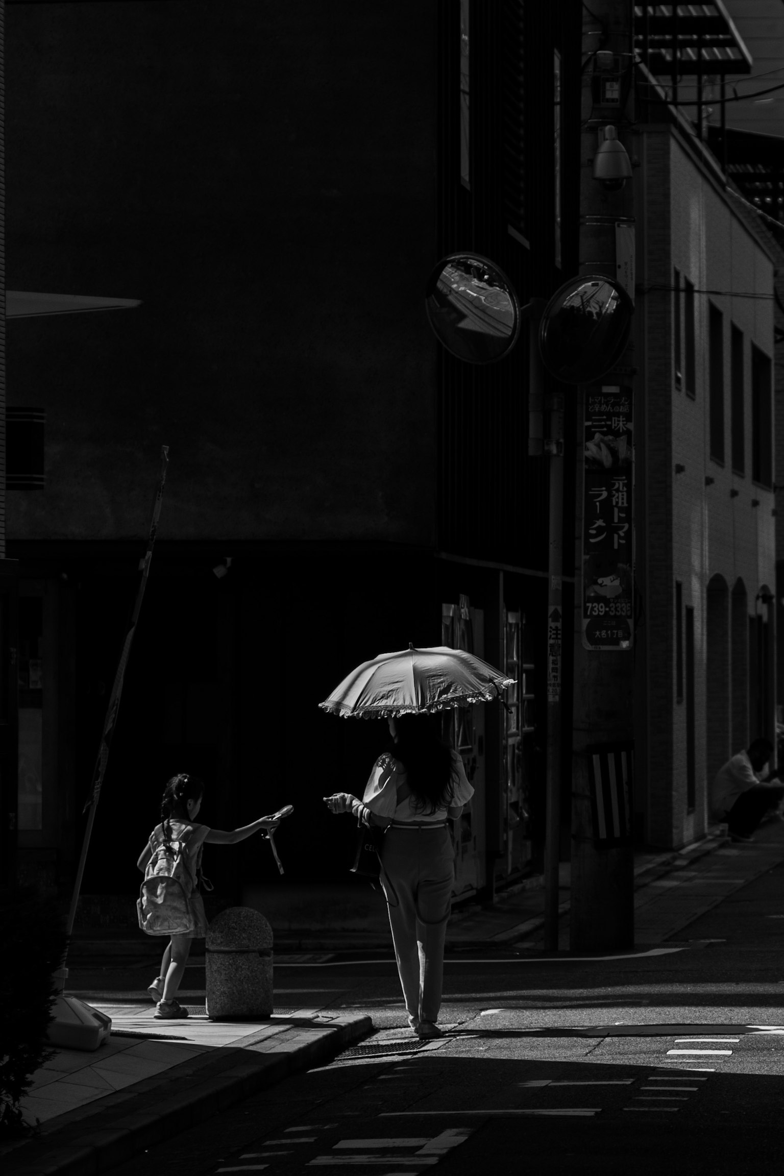 Silhouette of a woman walking with an umbrella at a street corner with a child