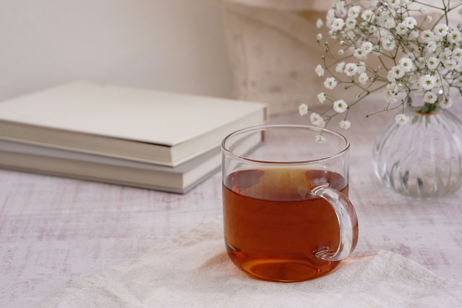 A clear cup of tea beside white books and small flowers on a calm table setting