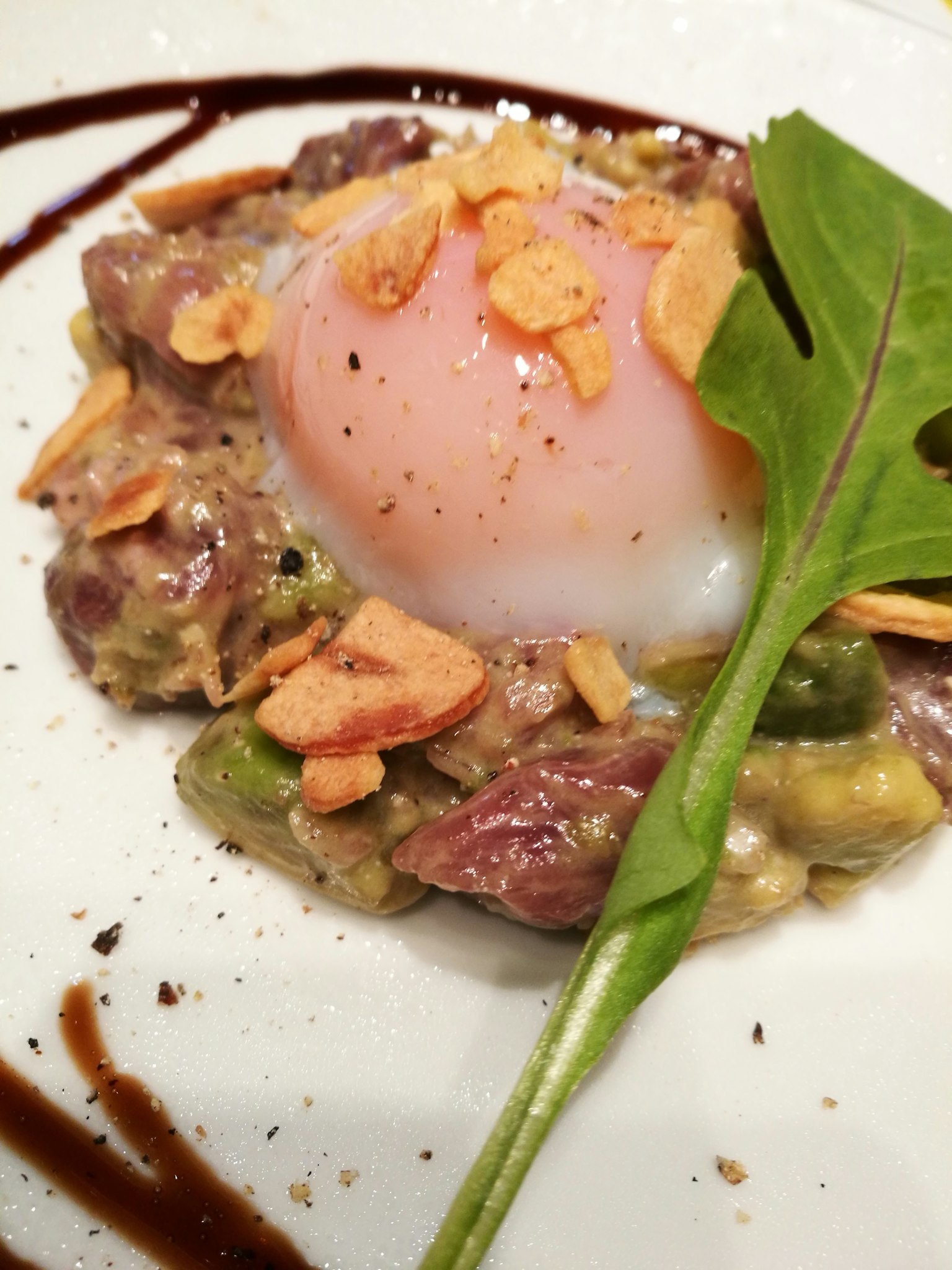 Un piatto con salsa cremosa, carne e uovo in camicia guarnito con mandorle e verdure