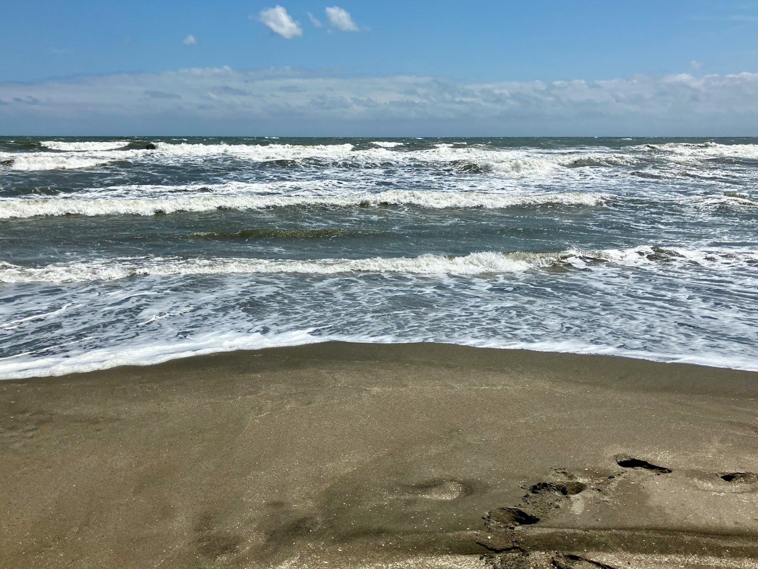 View of the ocean with waves sandy beach footprints blue sky and white clouds