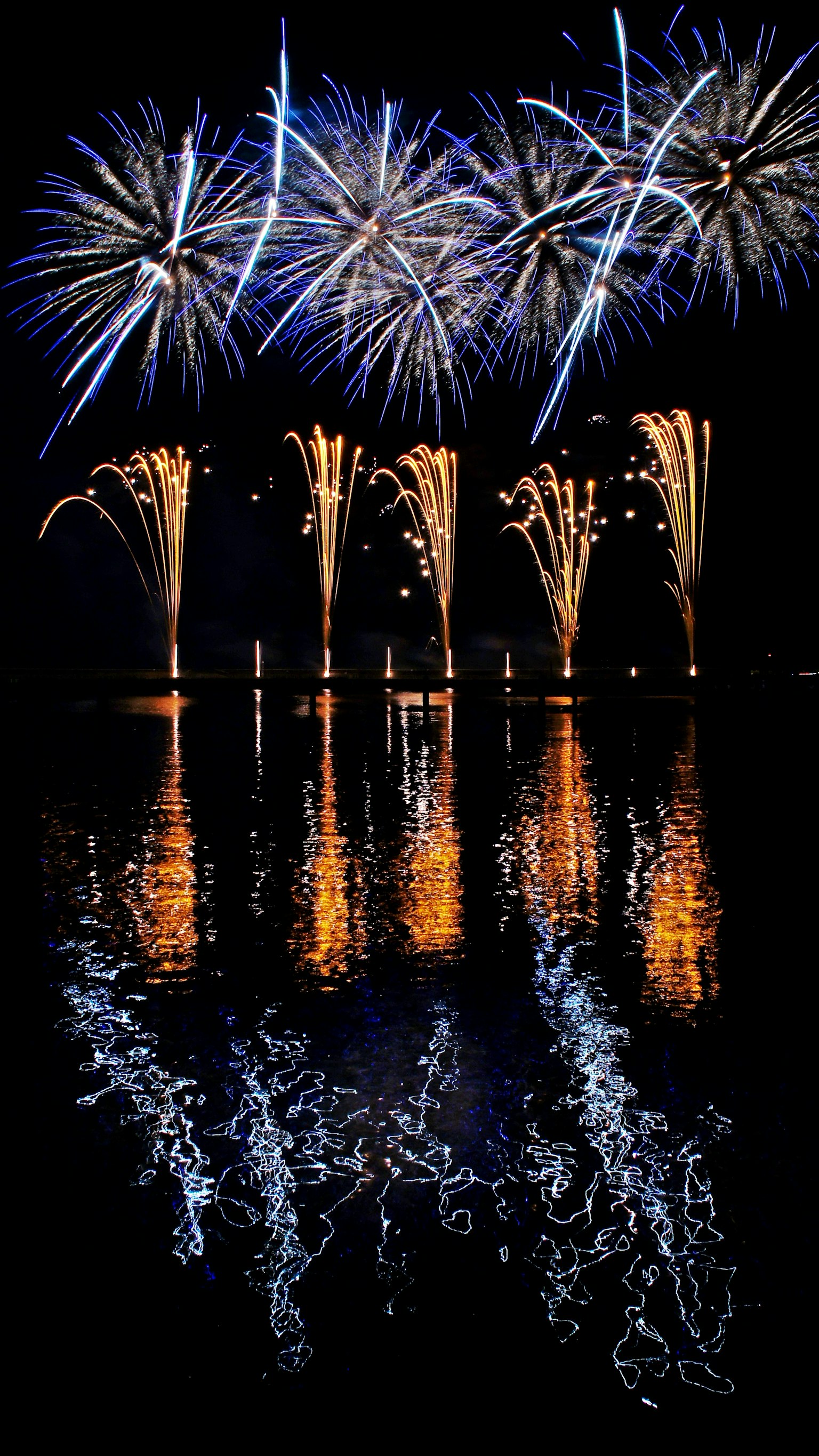 Spettacolo di fuochi d'artificio colorati nel cielo notturno con riflessi sulla superficie dell'acqua