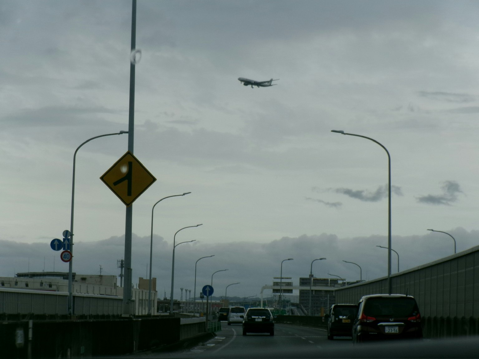 Mobil di jalan dekat bandara dengan pesawat terbang rendah di langit