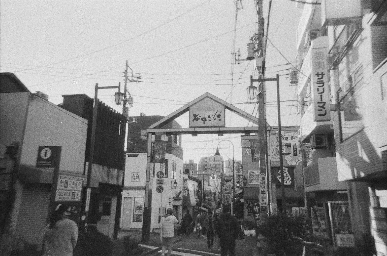 Escena urbana en blanco y negro con una calle concurrida y un letrero en arco