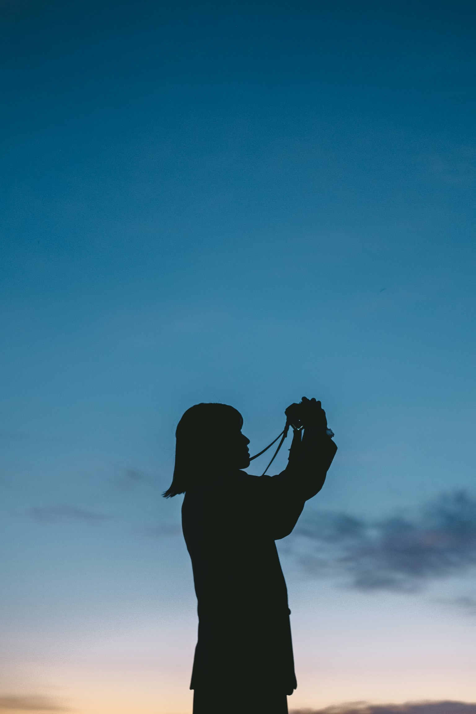 Silhouette di una persona che tiene una macchina fotografica contro un cielo al tramonto