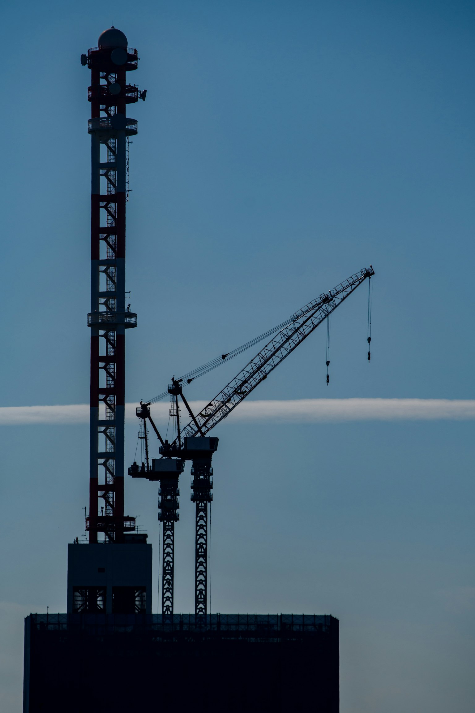 Silueta de una grúa y una torre de construcción contra un cielo azul