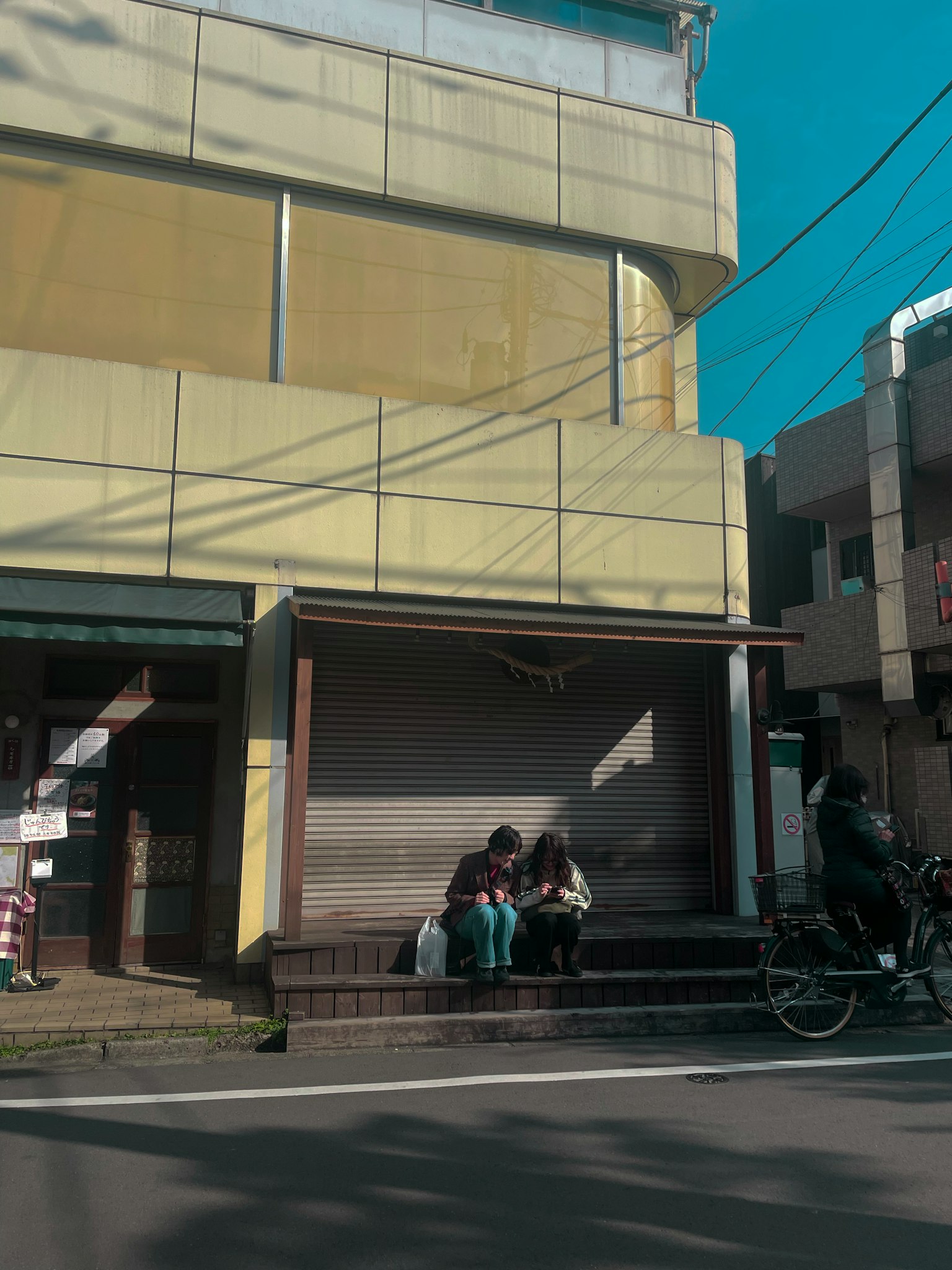 Street scene featuring a yellow building and two people sitting on a bench