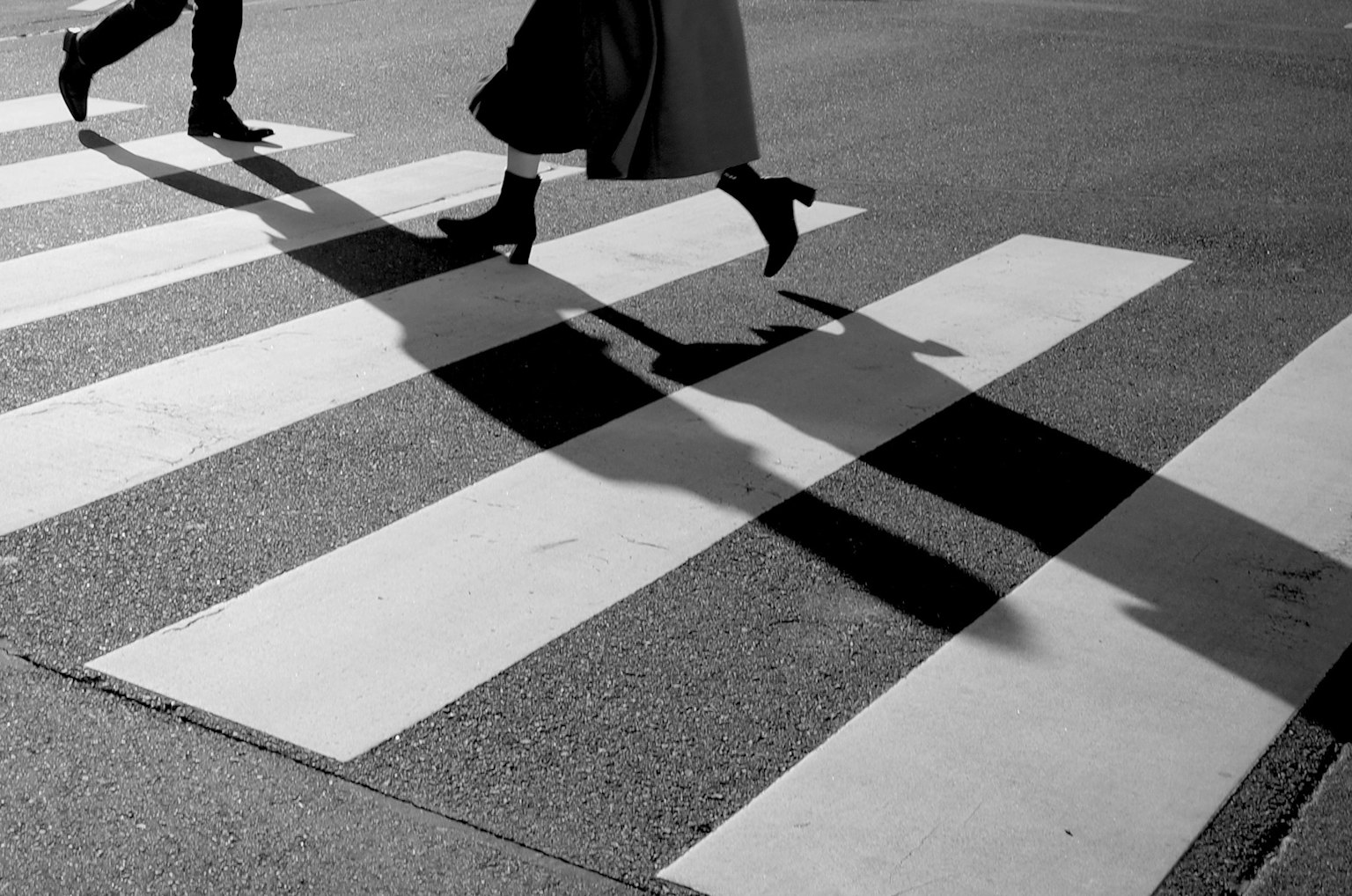 Feet walking on a black and white crosswalk with shadows