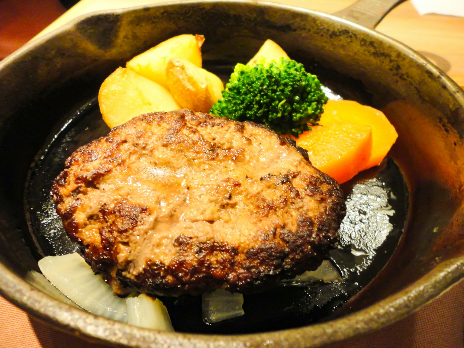 Zischendes Hamburgersteak auf einem heißen Teller mit Gemüse serviert