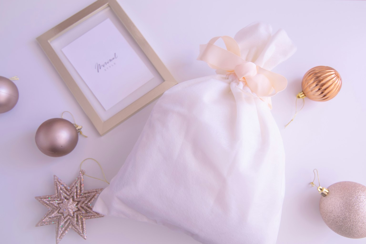 White fabric bag tied with a ribbon surrounded by Christmas ornaments and a frame