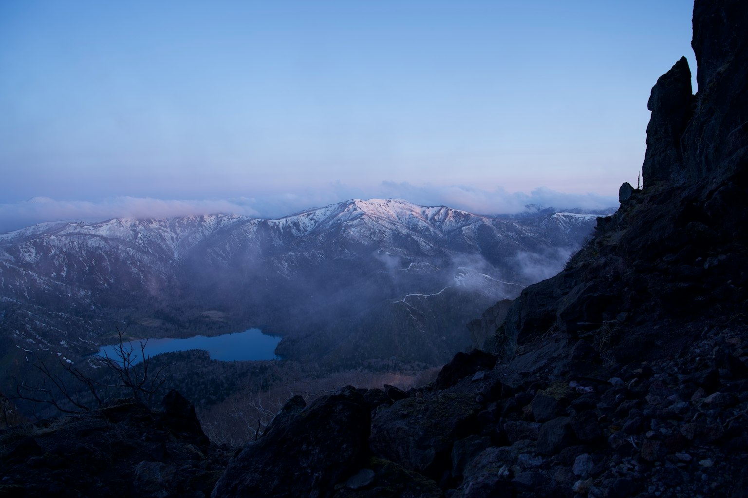 Un paisaje con cielo azul y montañas cubiertas de nieve Varias texturas de roca con un lago sereno visible