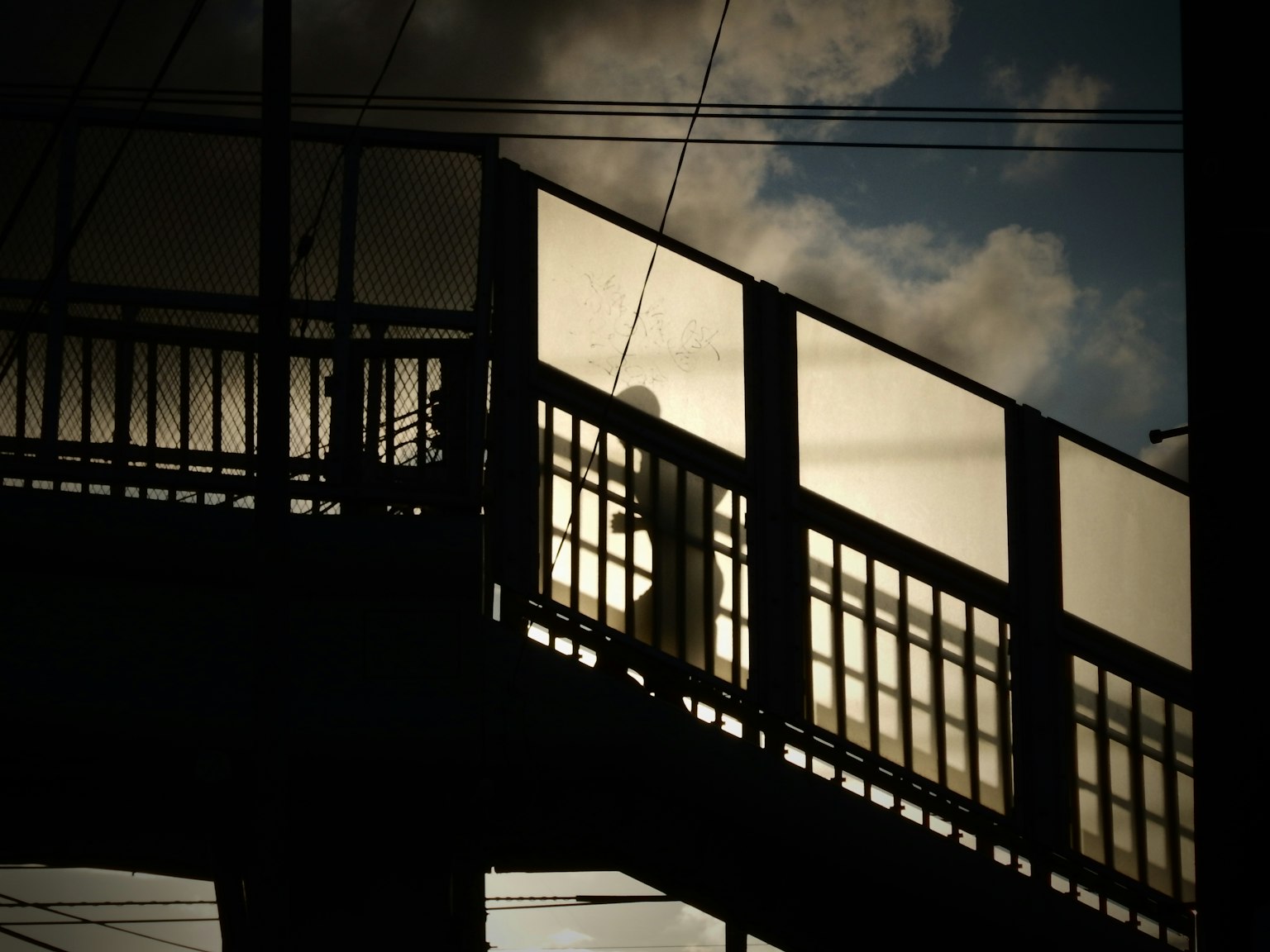 Silhouette of a person walking on a bridge with clouds in the background