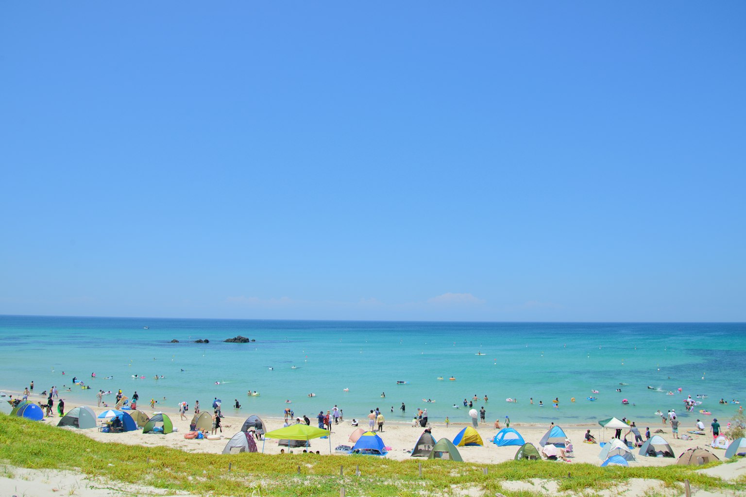 Pemandangan pantai dengan banyak orang menikmati hari yang cerah di bawah langit biru yang jelas dan air pirus